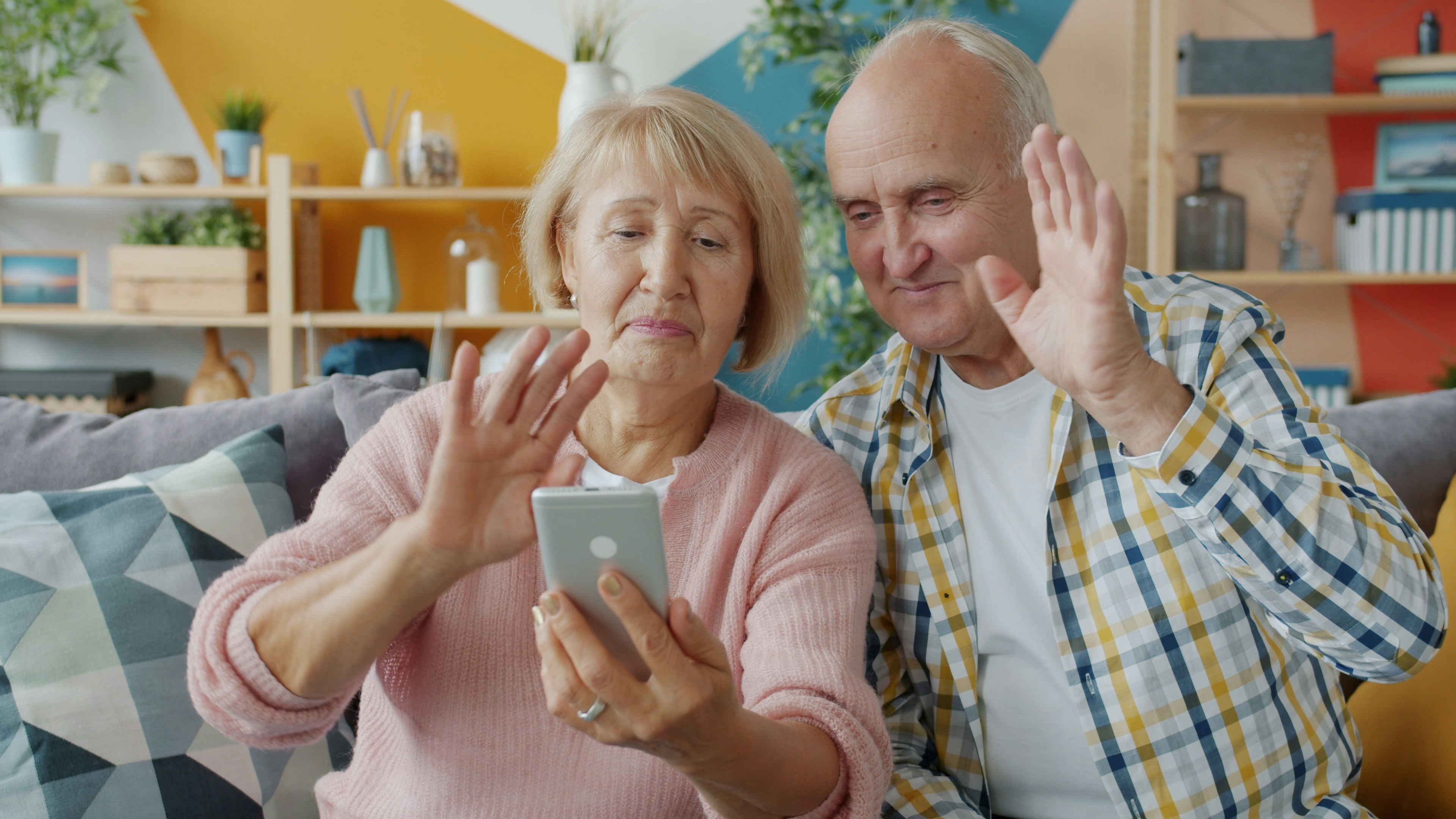 Couple de seniors souriant en appel vidéo avec leur famille depuis leur salon